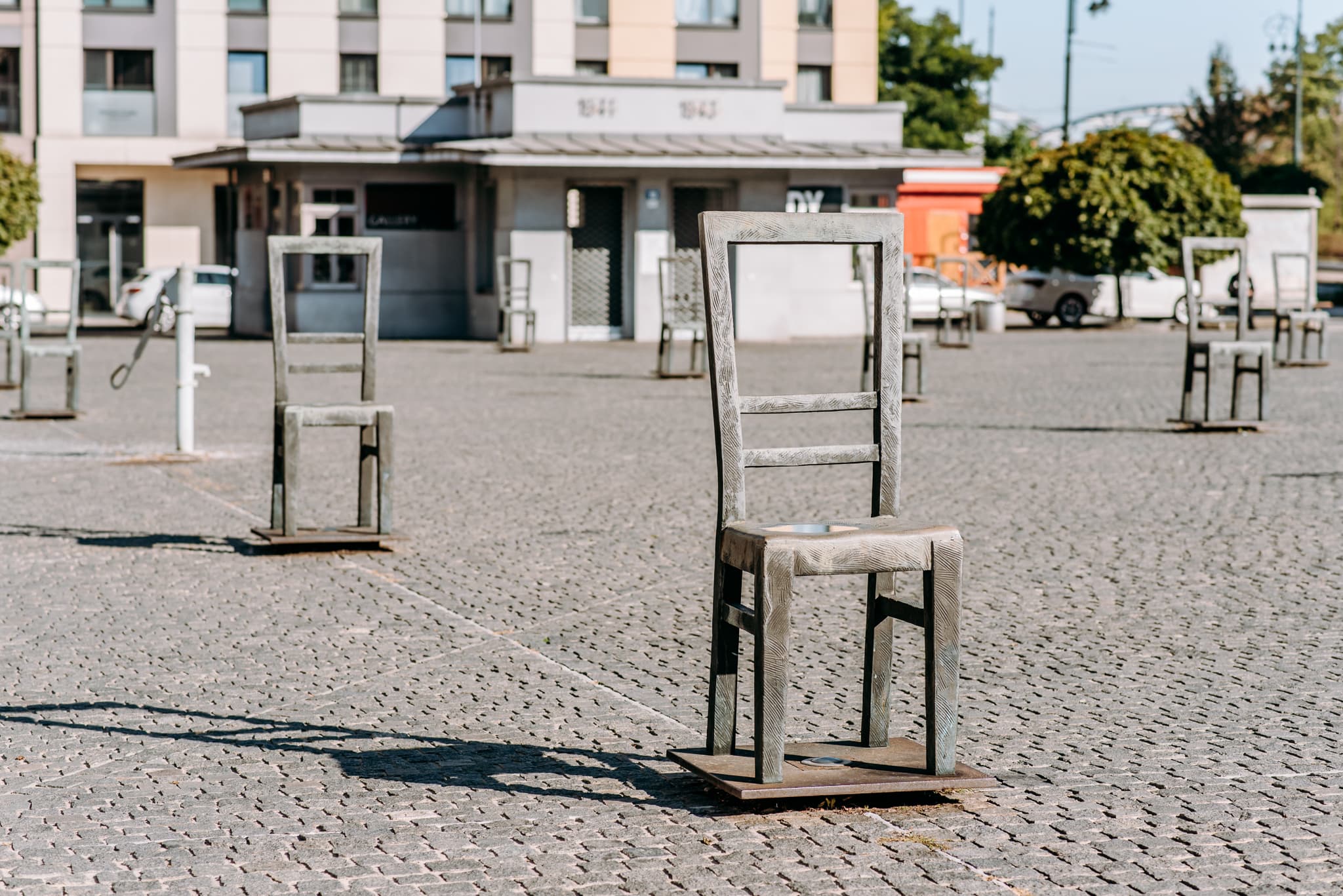 Art installation of wooden chairs on a cobblestone plaza with buildings in background.