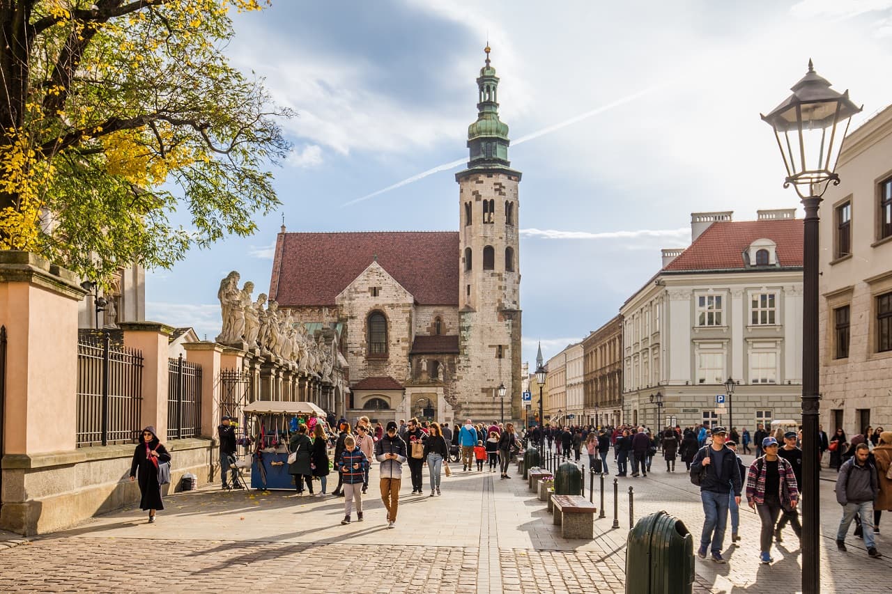 Busy street scene with people walking near historic church and autumn trees.