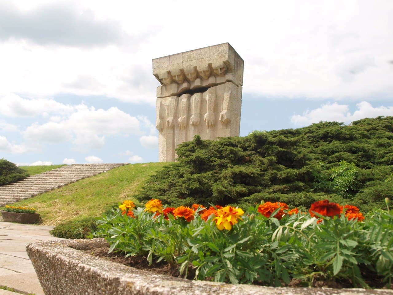 Stone monument surrounded by vibrant flowers and greenery under a cloudy sky.
