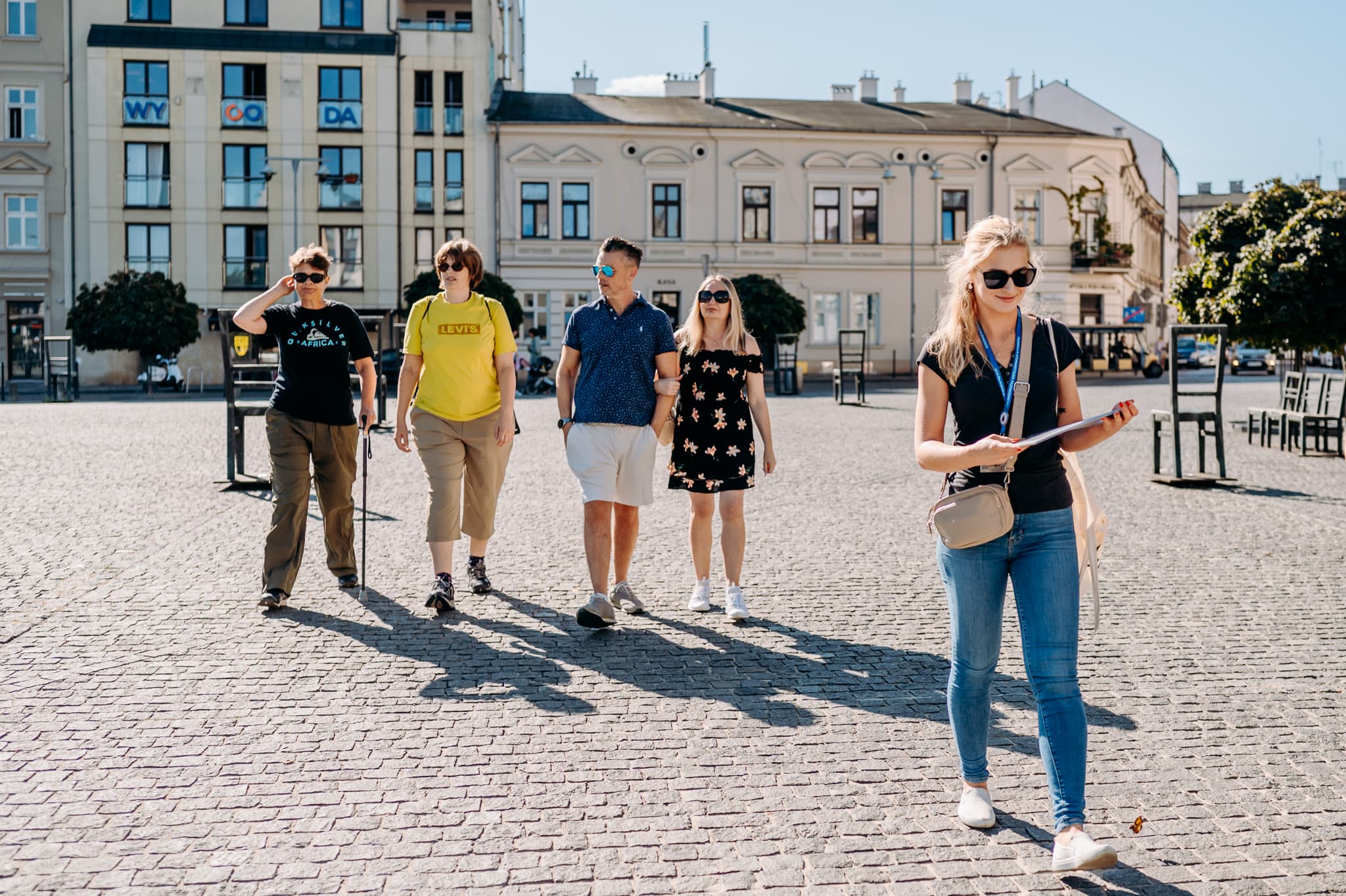 Group walking on a cobblestone plaza with historic buildings under clear blue sky.