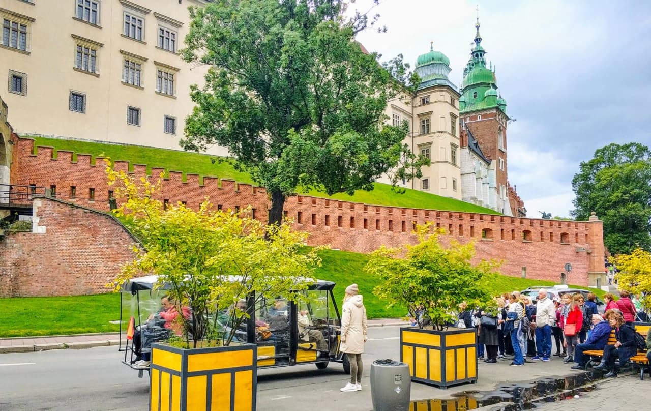 Tourists near castle walls with electric vehicles and greenery.