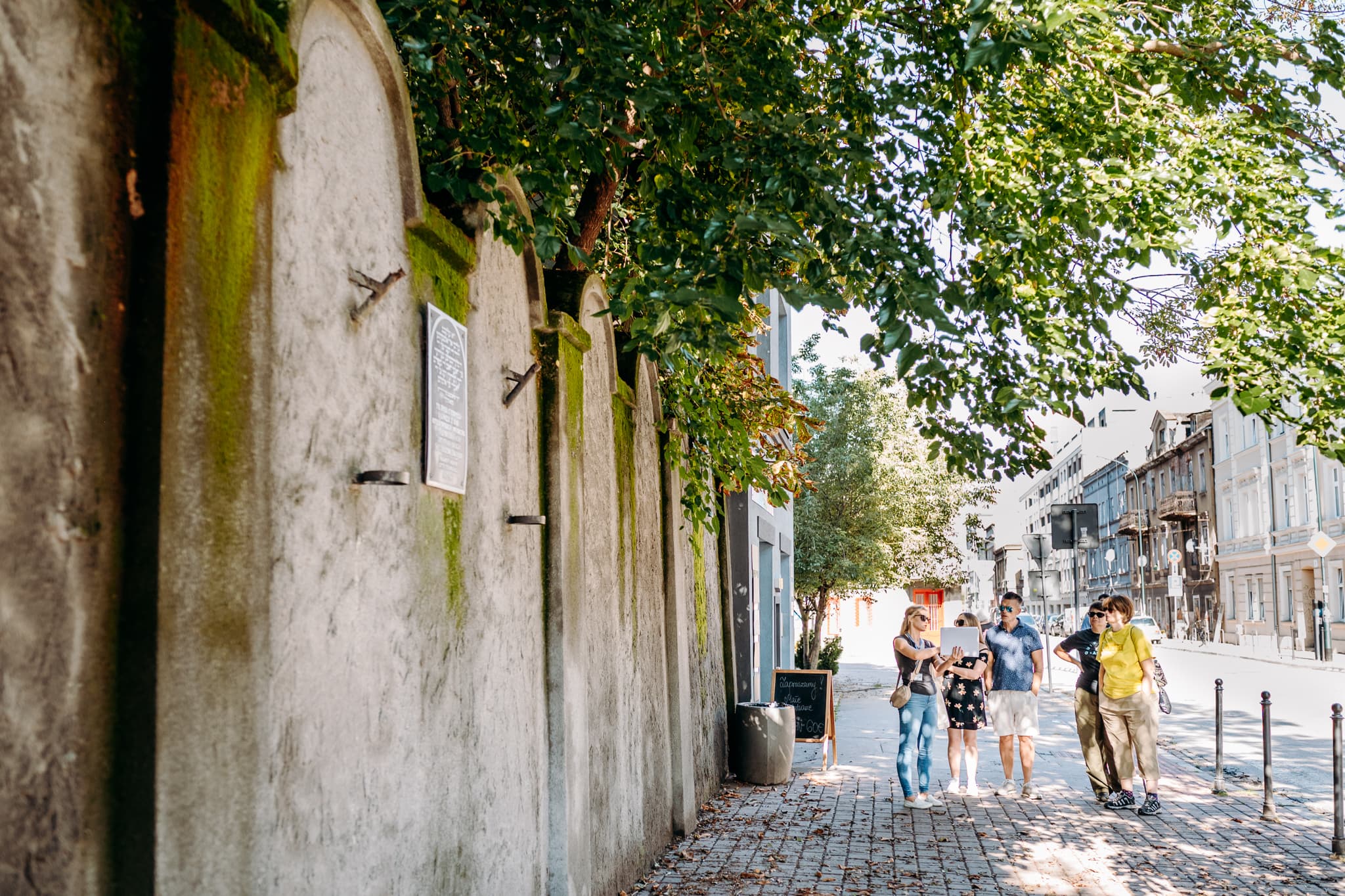 Group walking along a cobblestone path beside a moss-covered wall and trees.